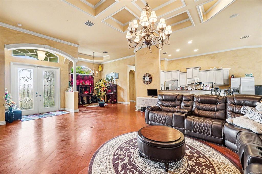 A spacious living room features a large leather sectional, a chandelier, and hardwood flooring — 20831 COPPERHEAD DRIVE, LEHIGH ACRES, FL
