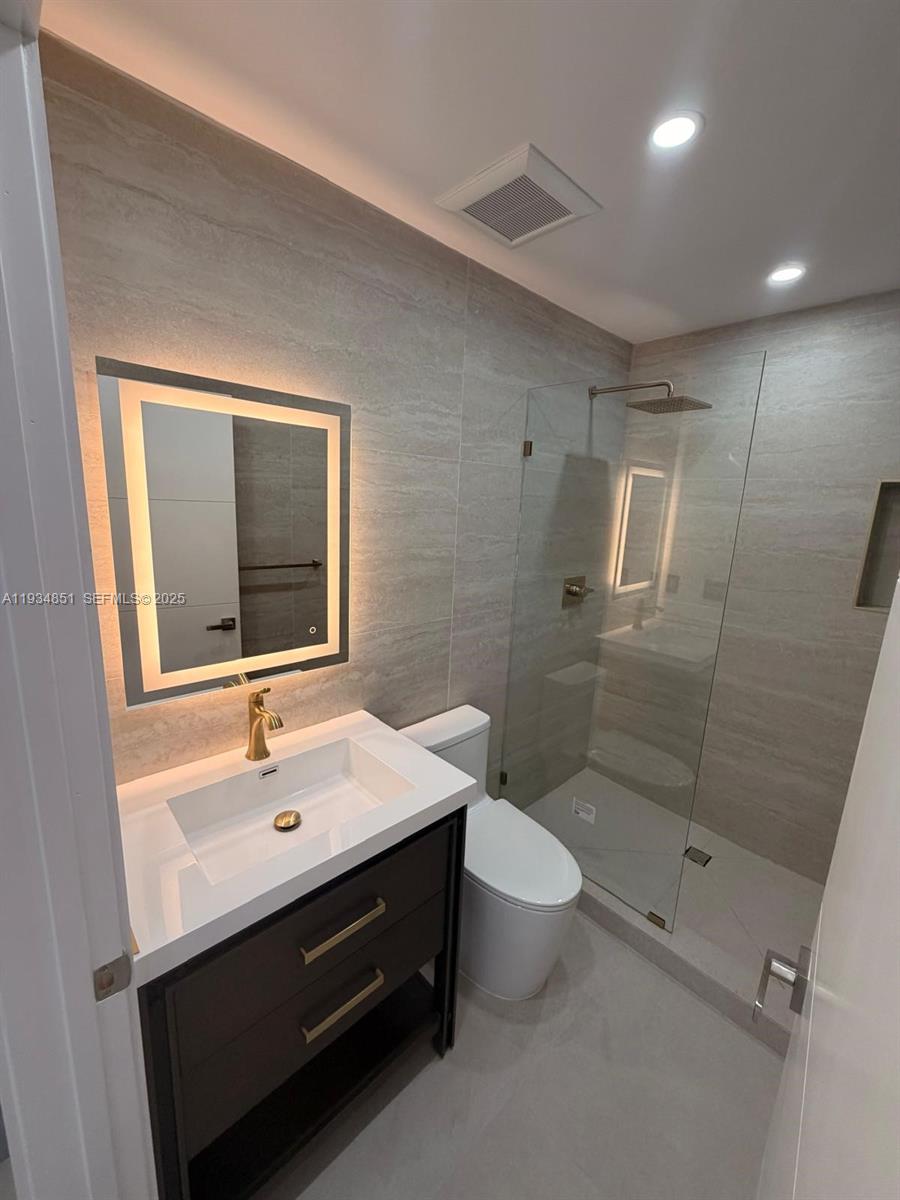 A modern bathroom features a dark vanity, gold faucet, illuminated mirror, and a glass shower — 2436 SW 7th St # 4, Miami FL 33135, MIAMI, FL