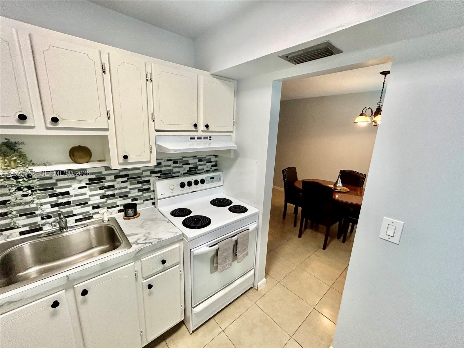 A kitchen with white cabinets, a tiled backsplash, and a white stove leads to a dining area — 2213 NE 1st Ct # 203, Boynton Beach FL 33435, BOYNTON BEACH, FL