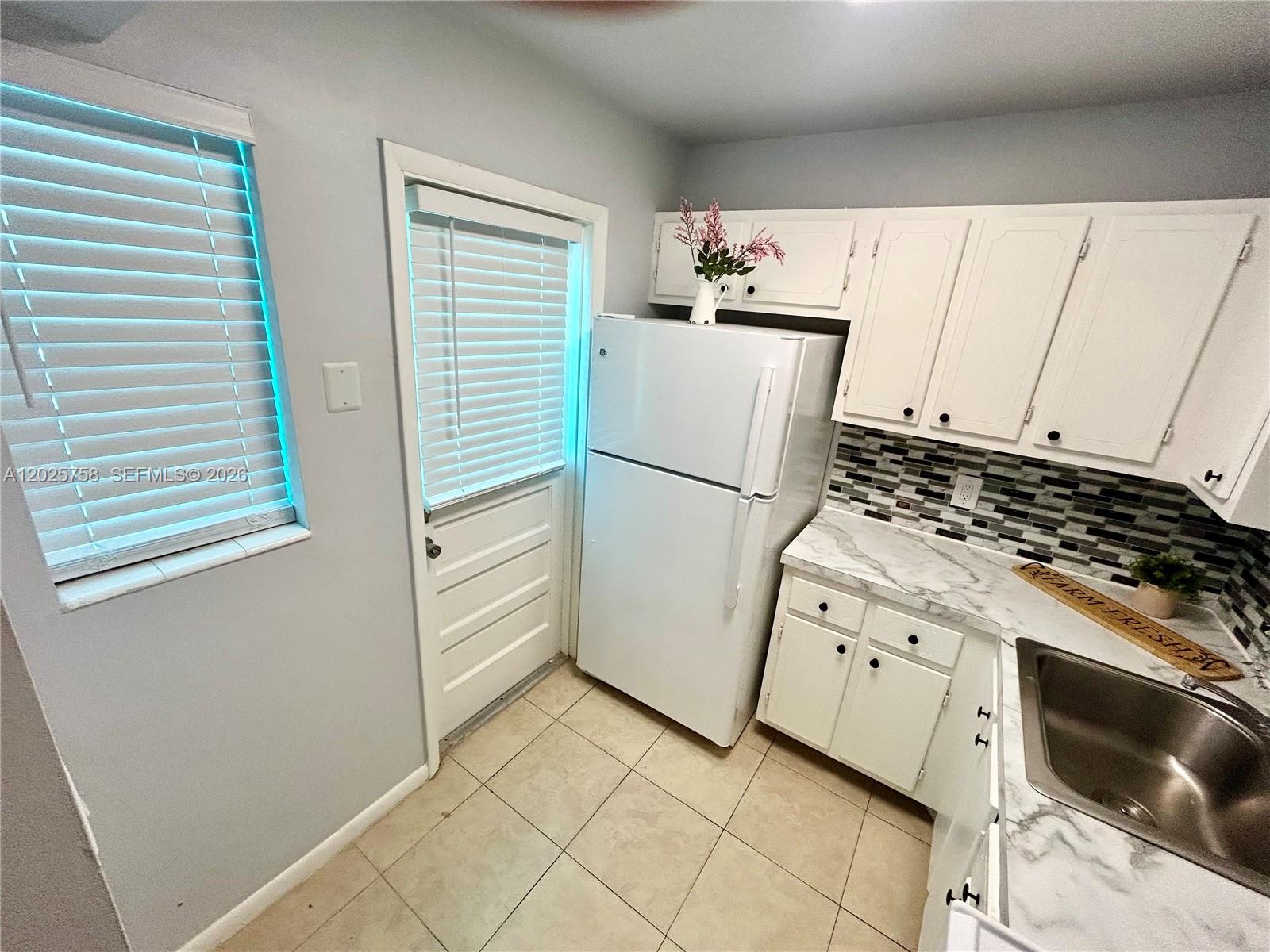 A kitchen features white cabinets, a white refrigerator, a marble-patterned countertop, and tiled flooring — 2213 NE 1st Ct # 203, Boynton Beach FL 33435, BOYNTON BEACH, FL