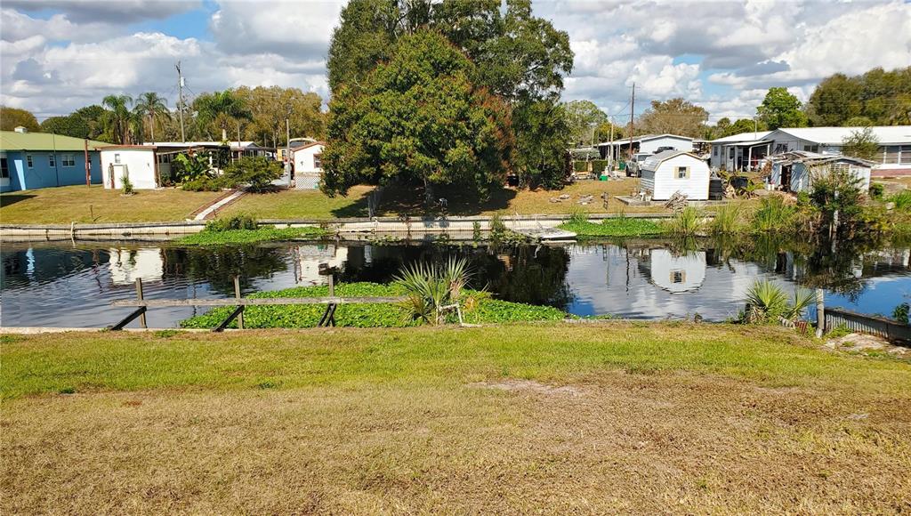 A grassy yard overlooks a narrow canal lined with vegetation and several small residential buildings — 3431 SE 28TH STREET, OKEECHOBEE, FL