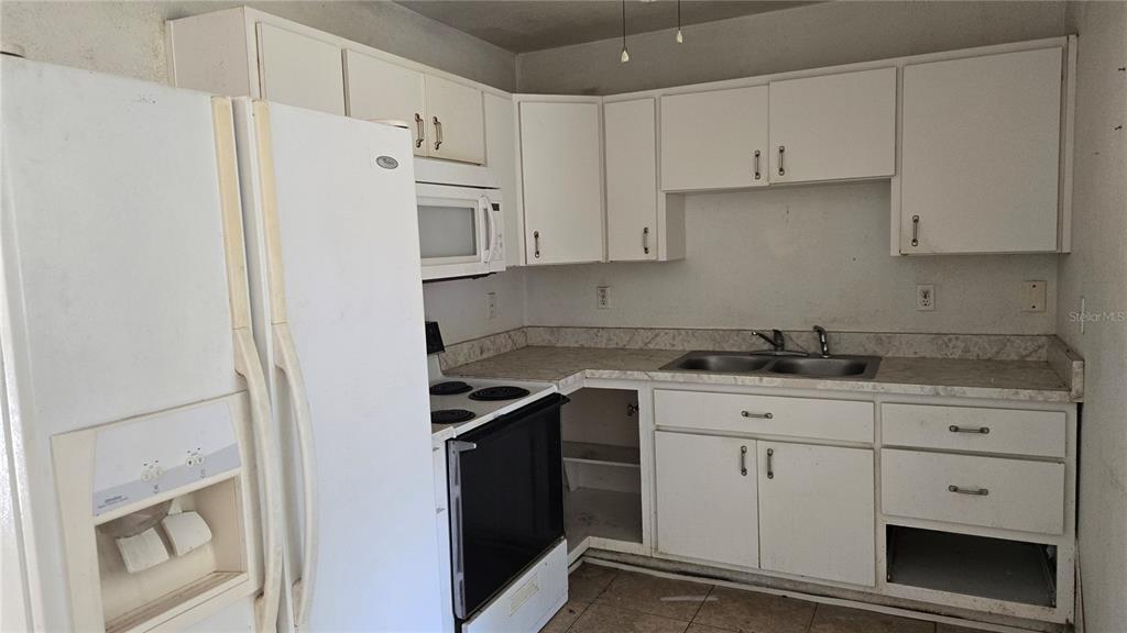 A kitchen features white cabinets, a white refrigerator, a black stove, and a double sink — 6404 SW 9TH AVENUE, OCALA, FL