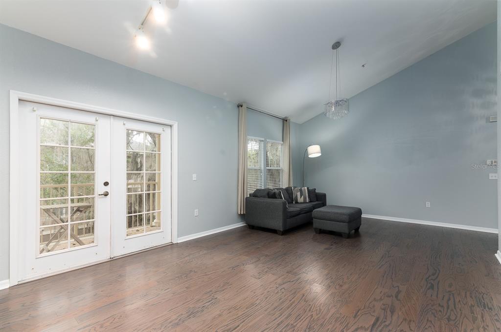 An empty living room with hardwood floors, vaulted ceilings, and an open kitchen — 4850 SW 91ST TERRACE UNIT 301, GAINESVILLE, FL