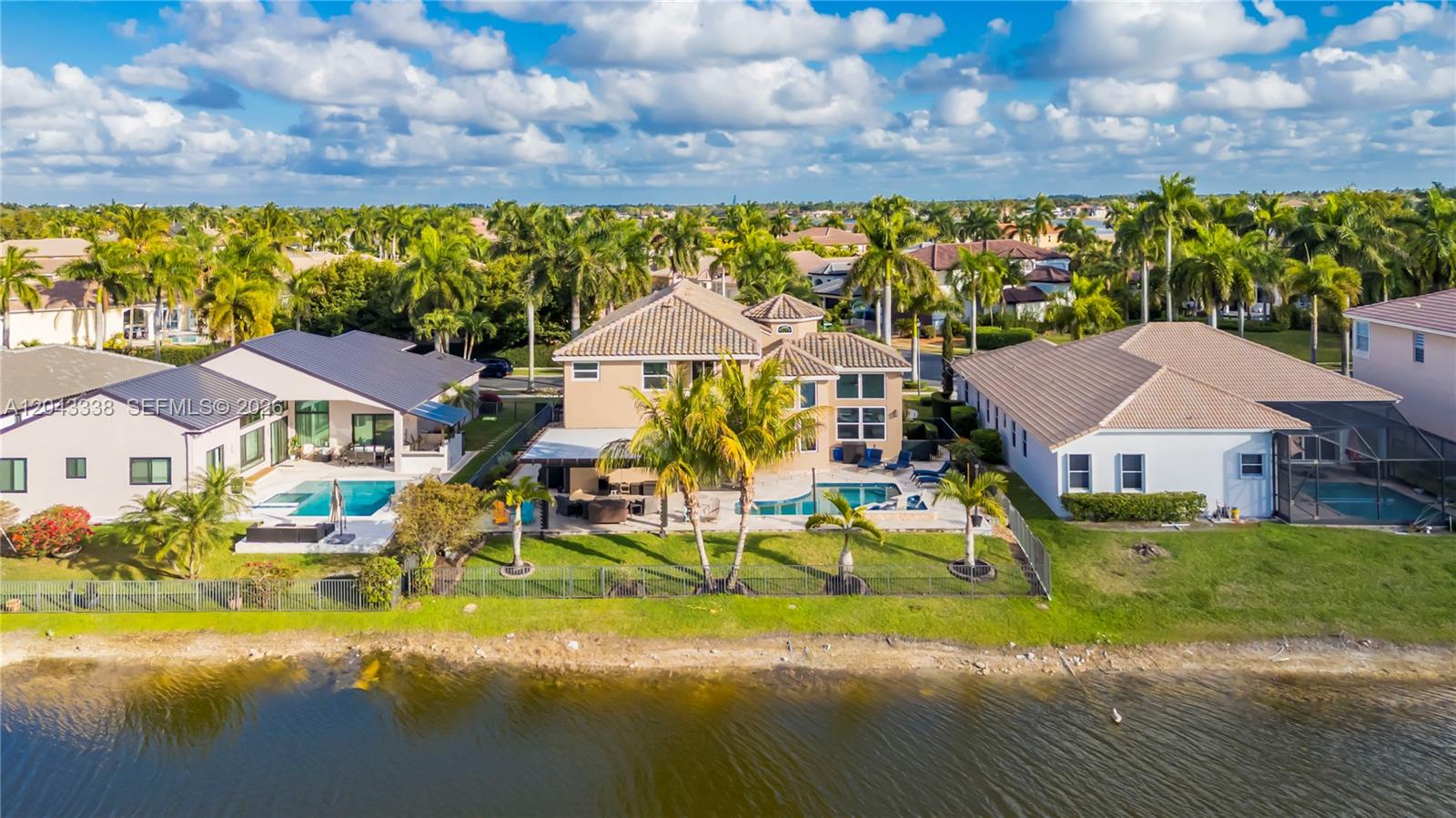 An aerial view shows three suburban houses with swimming pools situated along a lakefront — 3240 SW 190th Ave, Miramar FL 33029, MIRAMAR, FL