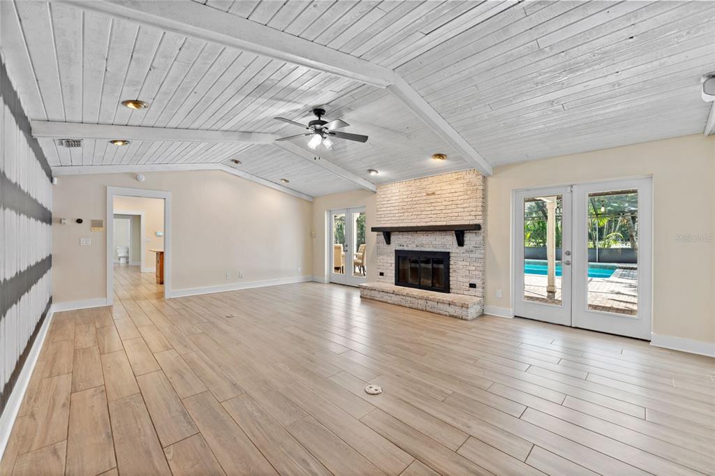 A spacious living room features a white vaulted wood ceiling, brick fireplace, and tile flooring — 2109 MEADOW BROOK DRIVE, CLEARWATER, FL
