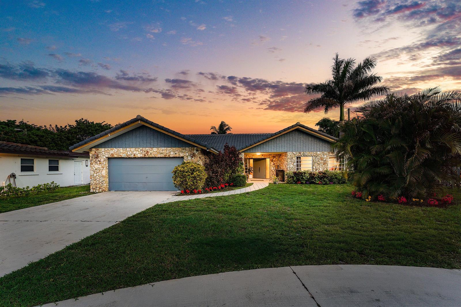 A single-story house with a stone facade, blue siding, and a concrete driveway at sunset — 1006 SE 6th Street, Deerfield Beach FL 33441, DEERFIELD BEACH, FL
