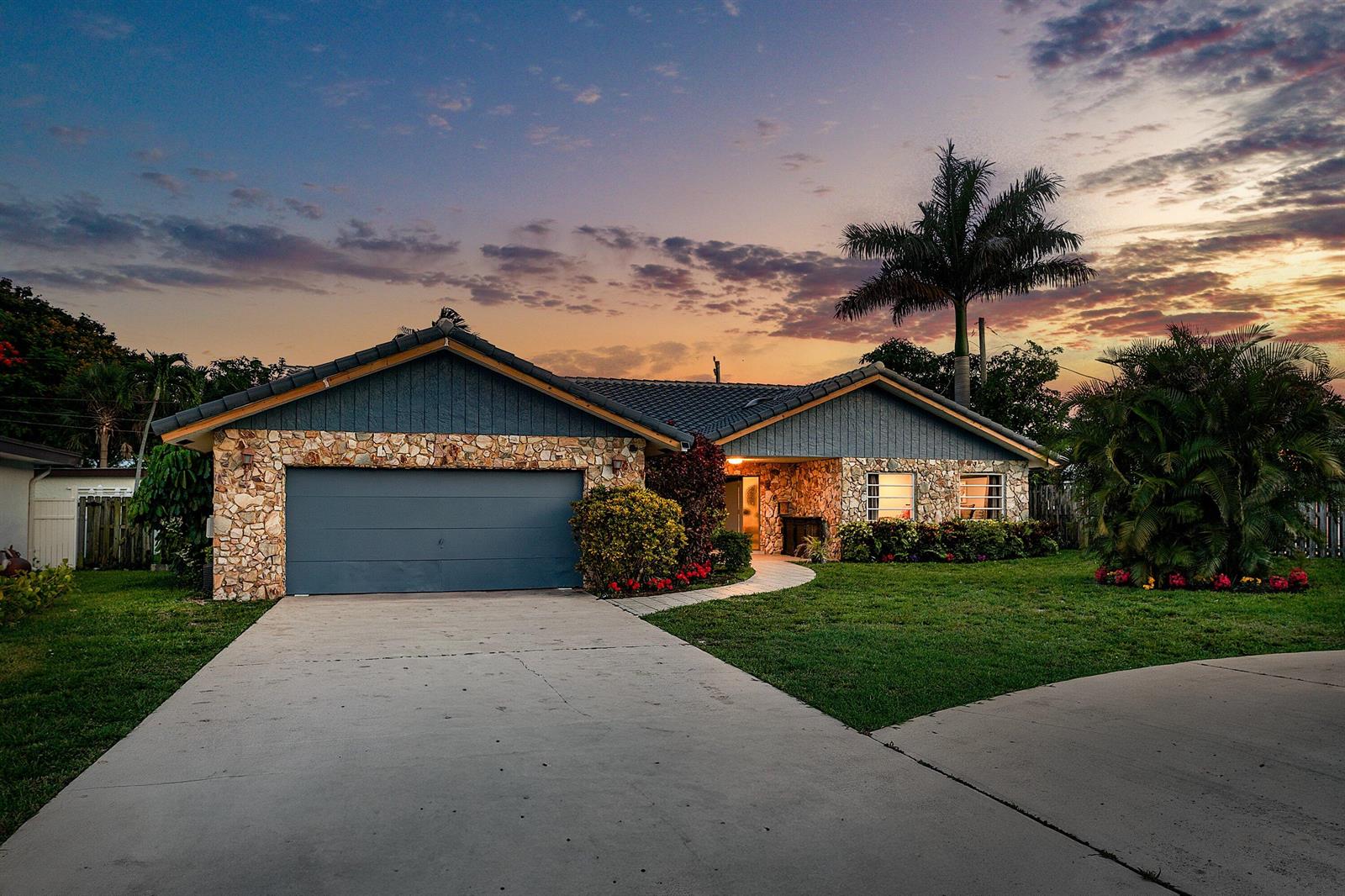 A single-story house with a stone facade, blue siding, and a concrete driveway at sunset — 1006 SE 6th Street, Deerfield Beach FL 33441, DEERFIELD BEACH, FL
