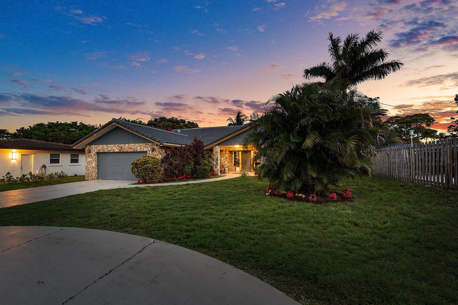 A single-story house with a stone facade, gray garage, and palm tree at sunset — 1006 SE 6th Street, Deerfield Beach FL 33441, DEERFIELD BEACH, FL