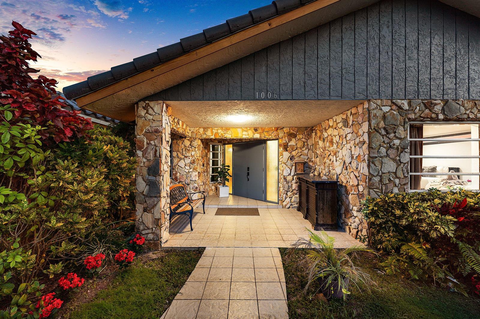 A stone-clad house entrance features a tiled walkway, a wooden bench, and double front doors — 1006 SE 6th Street, Deerfield Beach FL 33441, DEERFIELD BEACH, FL