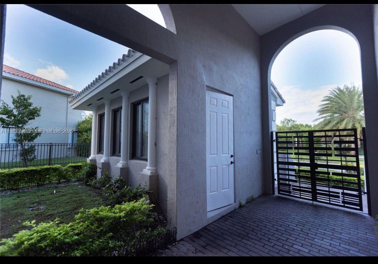 A paved side patio features a white door, arched entryway, and a black metal gate — 7408 SW 189th St, Cutler Bay FL 33157, CUTLER BAY, FL