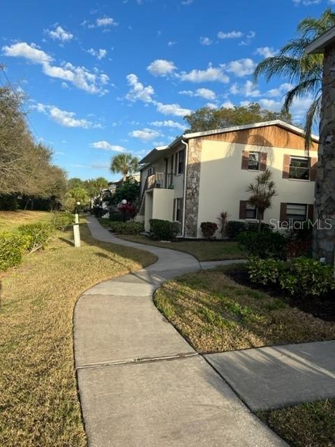 A concrete walkway leads toward a two-story apartment building with stone and stucco siding — 5400 34TH STREET W UNIT E8, BRADENTON, FL
