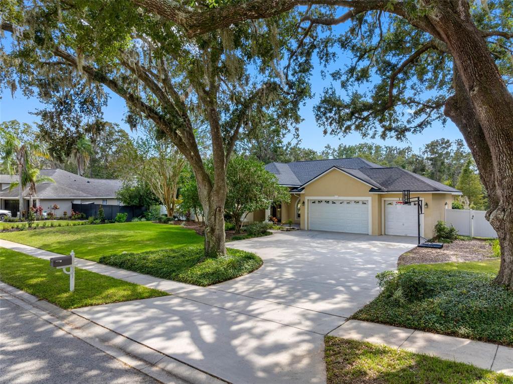 A tan single-story house with a three-car garage and large oak trees in the yard — 121 MYRTLE RIDGE ROAD, LUTZ, FL