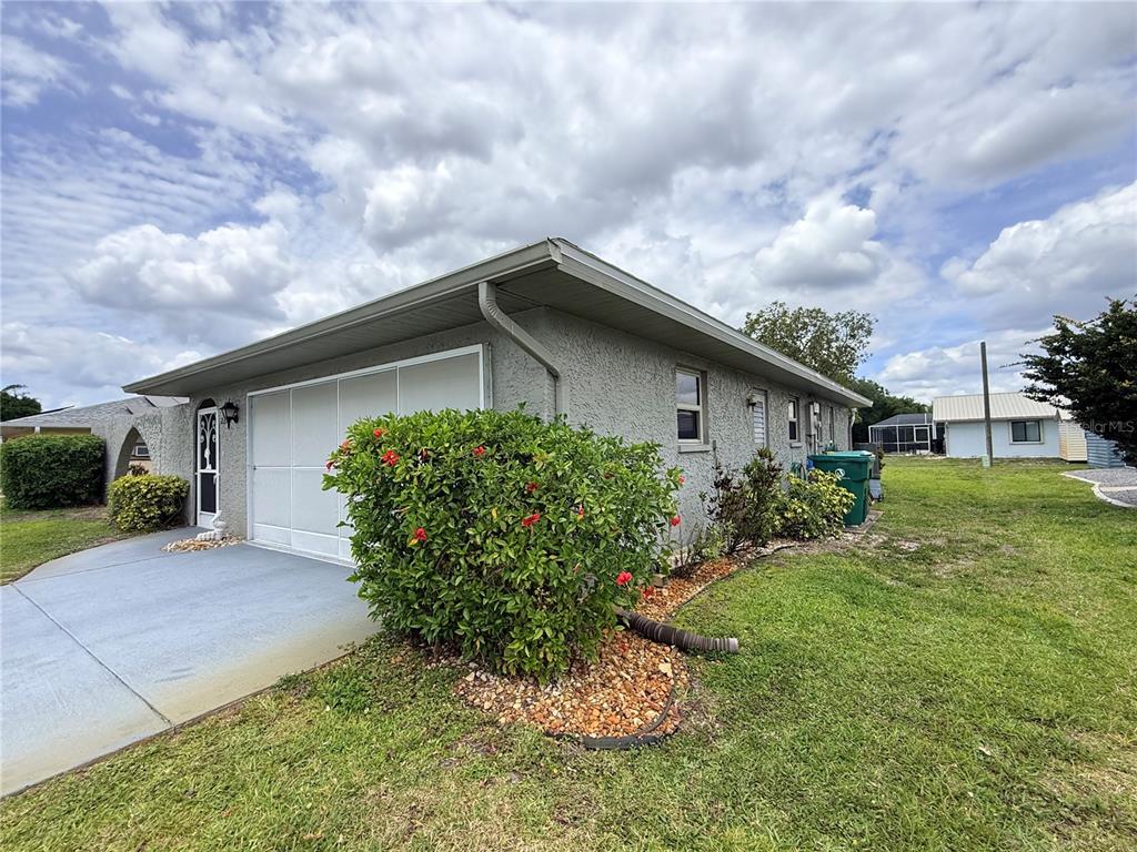 A side view of a gray stucco house with a garage and a large bush — 22506 GLEN AVENUE, PUNTA GORDA, FL