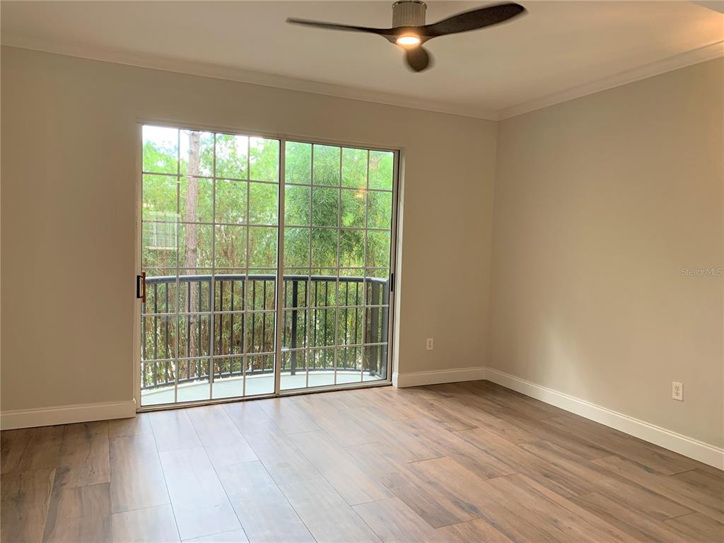 An empty room features wood-look flooring, a ceiling fan, and sliding glass doors to a balcony — 5208 HAMPTON BEACH PLACE UNIT 5208, TAMPA, FL