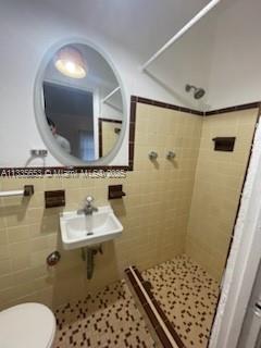 A bathroom features a wall-mounted sink, an oval mirror, and a tiled shower stall — 2811 Indian Creek Dr, Miami Beach FL 33140, MIAMI BEACH, FL