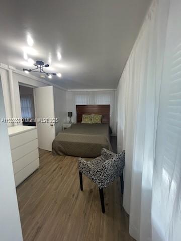 A bedroom features a bed, a white dresser, a patterned armchair, and light wood flooring — 2811 Indian Creek Dr, Miami Beach FL 33140, MIAMI BEACH, FL
