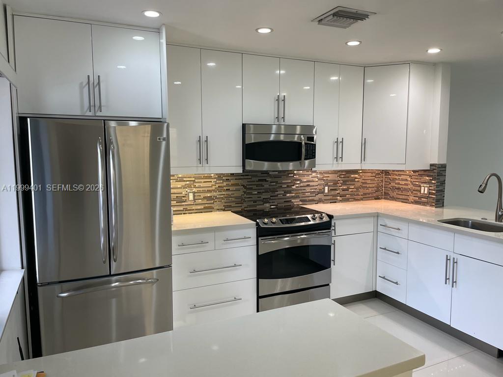 A modern kitchen features white cabinets, stainless steel appliances, and a mosaic tile backsplash — 454 Lakeview Dr # 2, Weston FL 33326, WESTON, FL