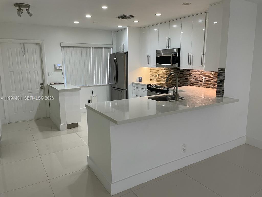 A modern kitchen features white cabinetry, stainless steel appliances, and a quartz-topped peninsula island — 454 Lakeview Dr # 2, Weston FL 33326, WESTON, FL