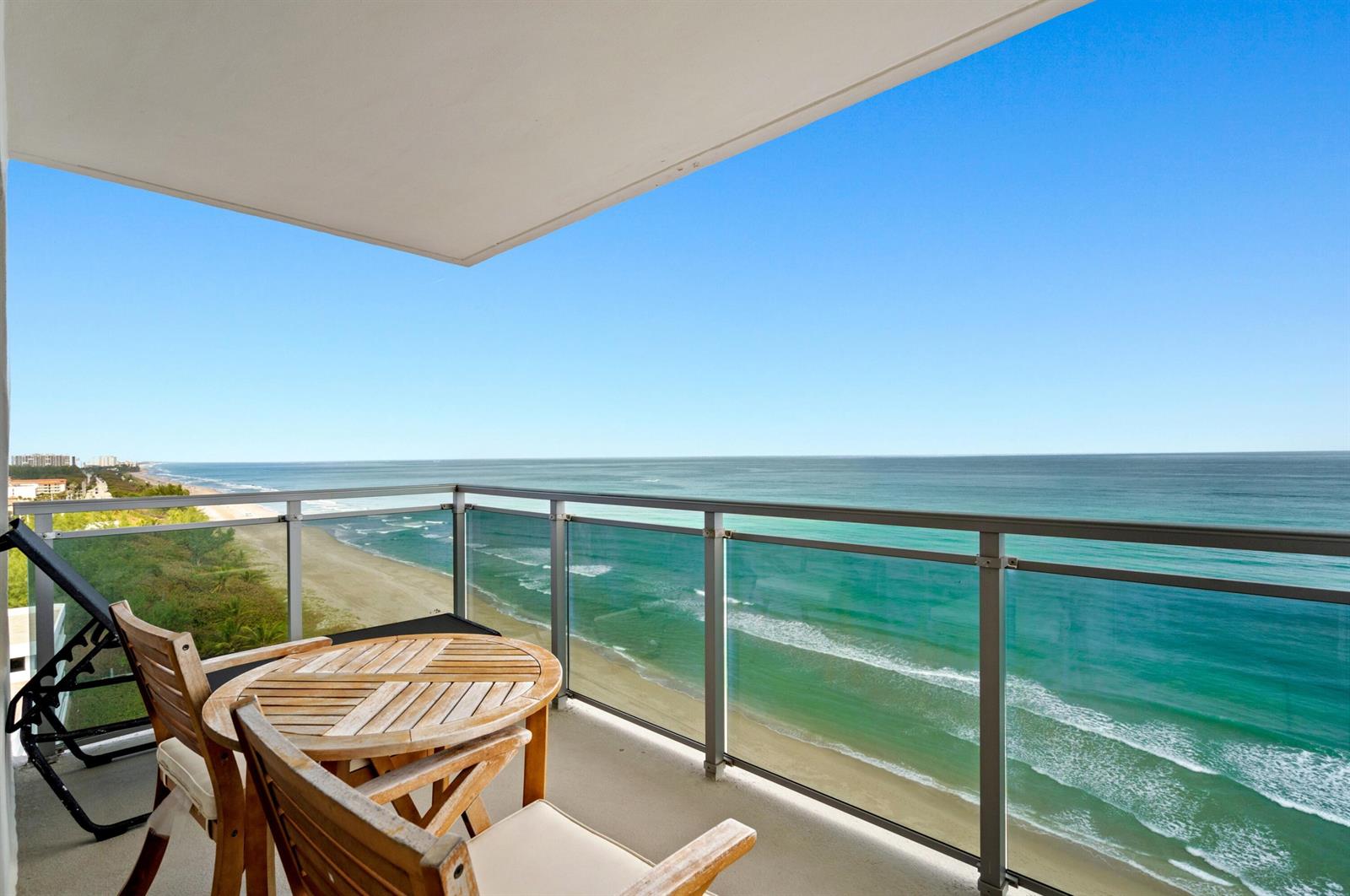 A balcony with wooden furniture overlooks a sandy beach and the turquoise ocean — 2066 N Ocean Boulevard, Boca Raton FL 33431, BOCA RATON, FL