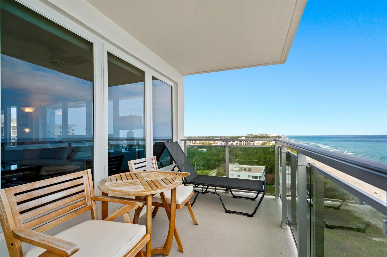 A balcony with wooden furniture and a lounge chair overlooks the ocean and coastline — 2066 N Ocean Boulevard, Boca Raton FL 33431, BOCA RATON, FL