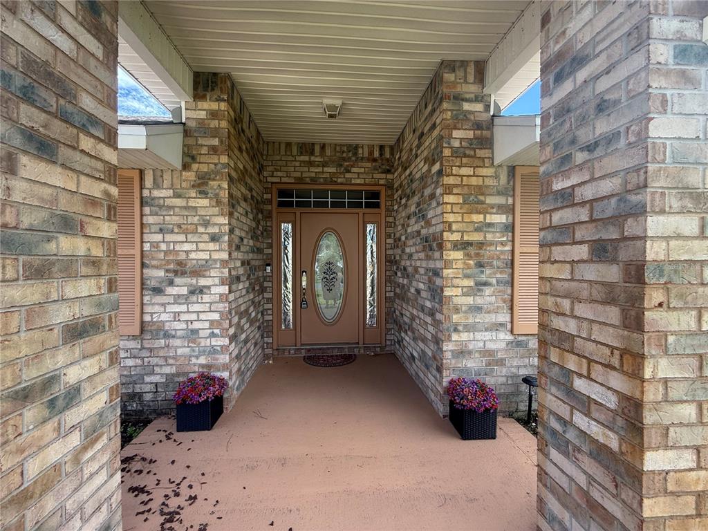 A brick-walled entryway features a tan front door with a glass oval insert and sidelights — 4 BALLARD LANE, PALM COAST, FL
