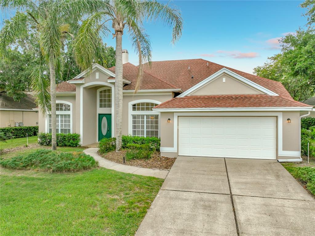 A single-story house with a tan stucco exterior, a two-car garage, and a green front door — 635 LONG LAKE DRIVE, OVIEDO, FL