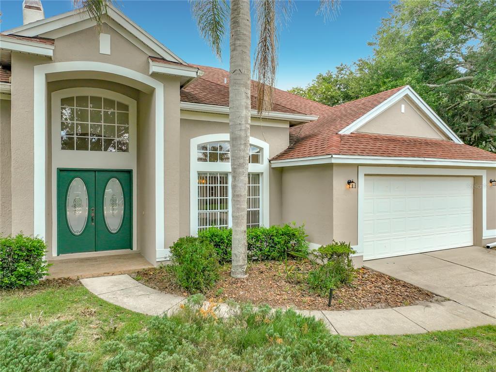 A tan house exterior features a green double front door, a garage, and a palm tree — 635 LONG LAKE DRIVE, OVIEDO, FL