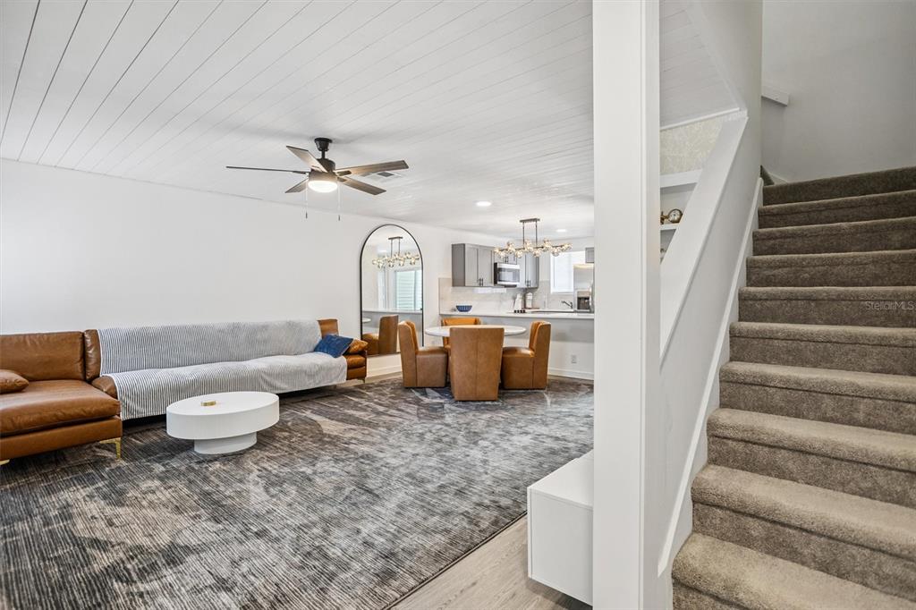 A living room with a brown sectional, dining area, and carpeted stairs leading upward — 4712 STONEPOINTE PLACE, TAMPA, FL