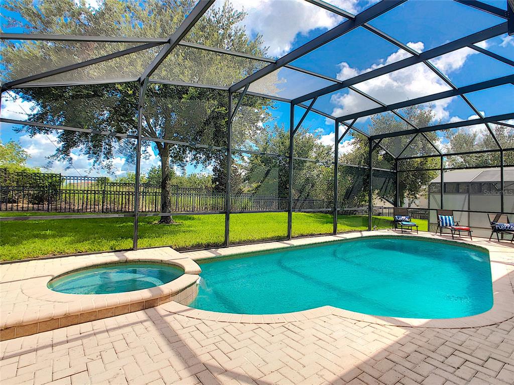 A screened-in pool and spa area with brick pavers and a grassy backyard — 7805 BEECHFIELD STREET, KISSIMMEE, FL