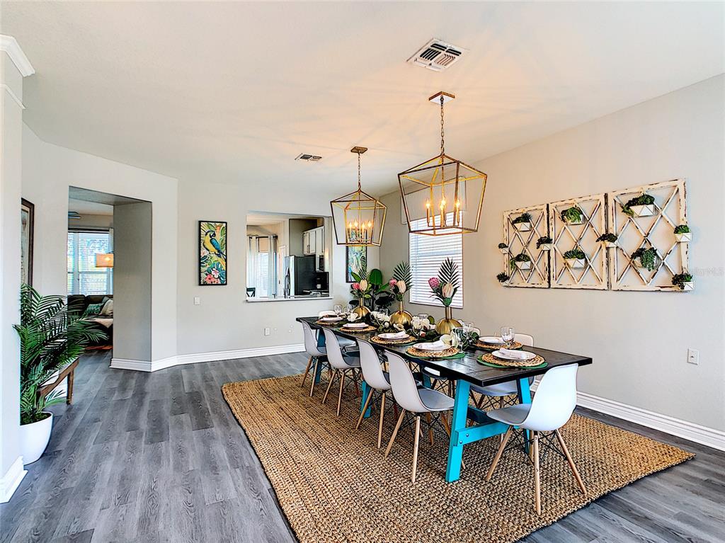 A dining room features a long table with teal legs, white chairs, and two pendant lights — 7805 BEECHFIELD STREET, KISSIMMEE, FL