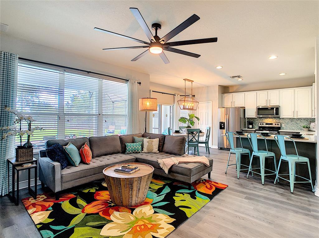 An open-concept living room and kitchen featuring a gray sectional, colorful rug, and island seating — 7805 BEECHFIELD STREET, KISSIMMEE, FL