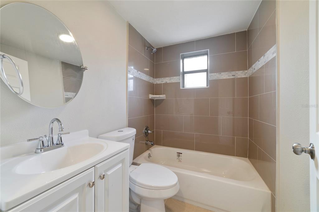 A bathroom features a white vanity, a toilet, and a bathtub with tan tiled walls — 2441 CHURCH STREET, SANFORD, FL