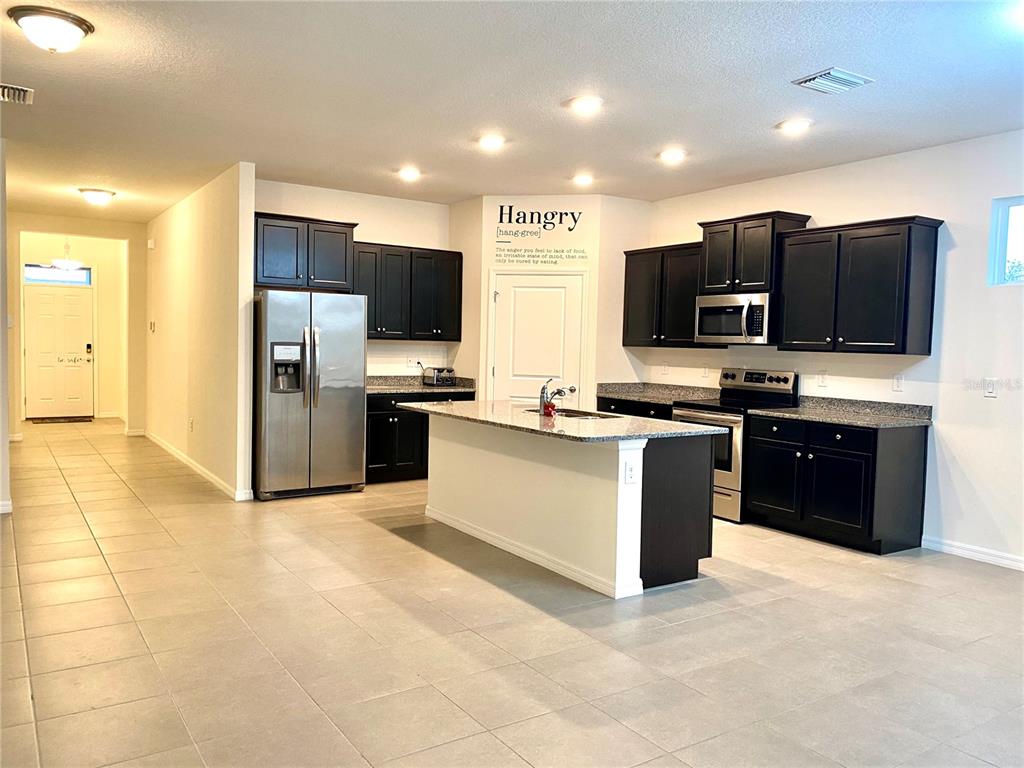 A kitchen features dark cabinetry, stainless steel appliances, a central island, and light tile flooring — 31882 TANSY BEND, WESLEY CHAPEL, FL