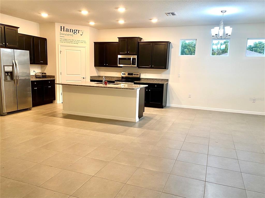 A kitchen features dark wood cabinets, granite countertops, a center island, and tile flooring — 31882 TANSY BEND, WESLEY CHAPEL, FL