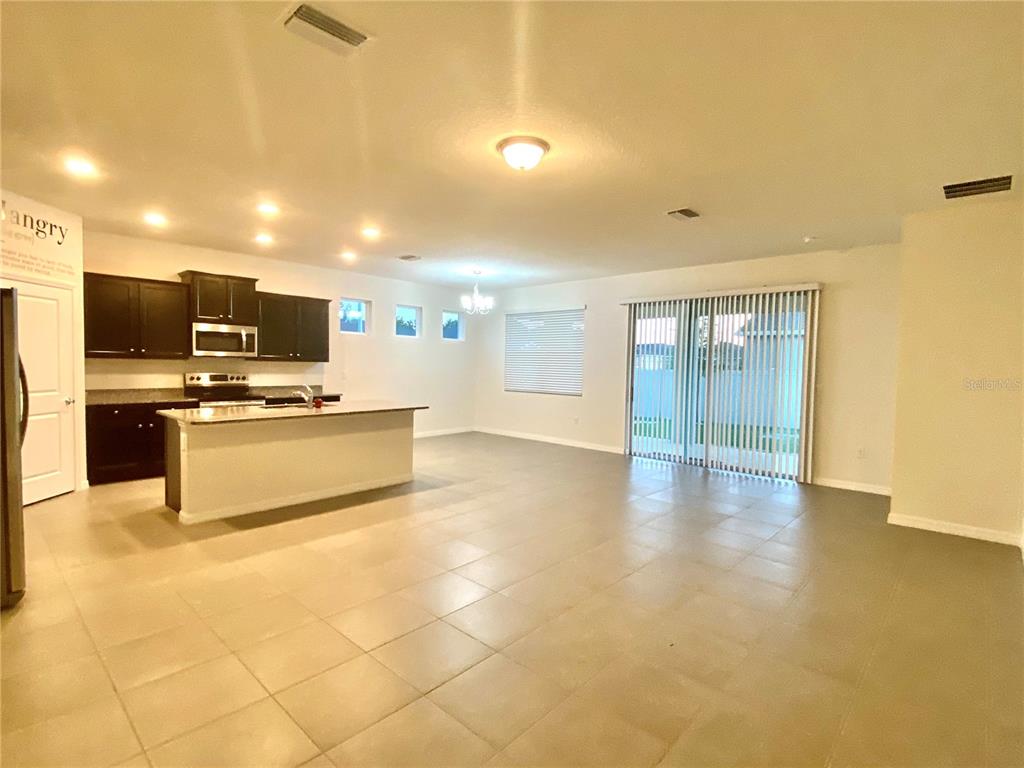 An open-concept kitchen and living area features dark cabinetry, a central island, and tile flooring — 31882 TANSY BEND, WESLEY CHAPEL, FL