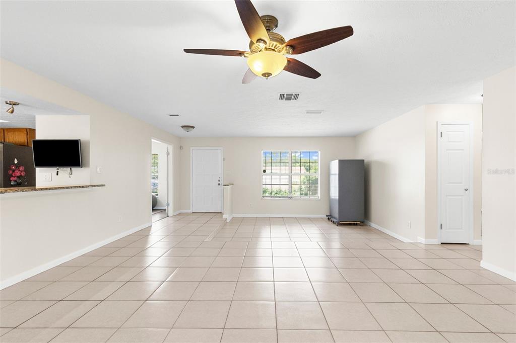 A spacious living area with light tile flooring, a ceiling fan, and a white door — 8904 W FLORA STREET, TAMPA, FL