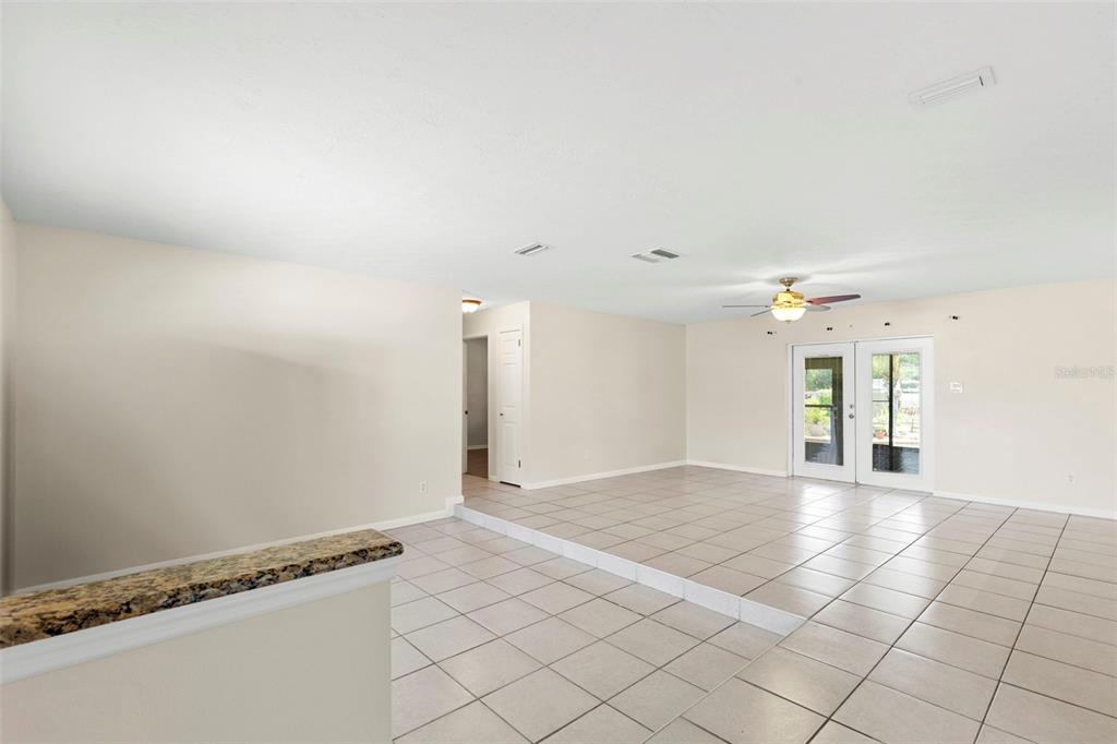 A living room with a raised tiled floor, a ceiling fan, and glass patio doors — 8904 W FLORA STREET, TAMPA, FL