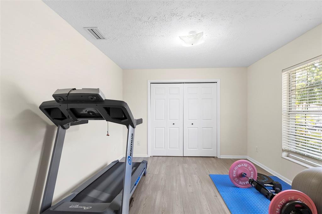 A room with light-colored walls, wood-look flooring, a treadmill, and exercise equipment on a mat — 8904 W FLORA STREET, TAMPA, FL