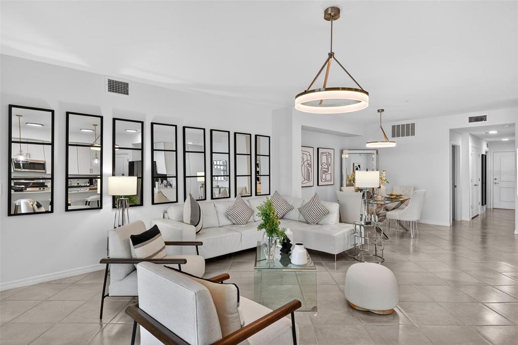A bright living room features a white sectional sofa, modern lighting, and a mirrored wall — 43250 WATER BIRD WAY UNIT 5911, PUNTA GORDA, FL