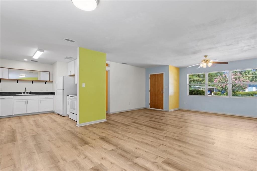 An open-concept living area with light wood flooring, a kitchen, and yellow accent walls — 1302 NE 14TH TERRACE, GAINESVILLE, FL