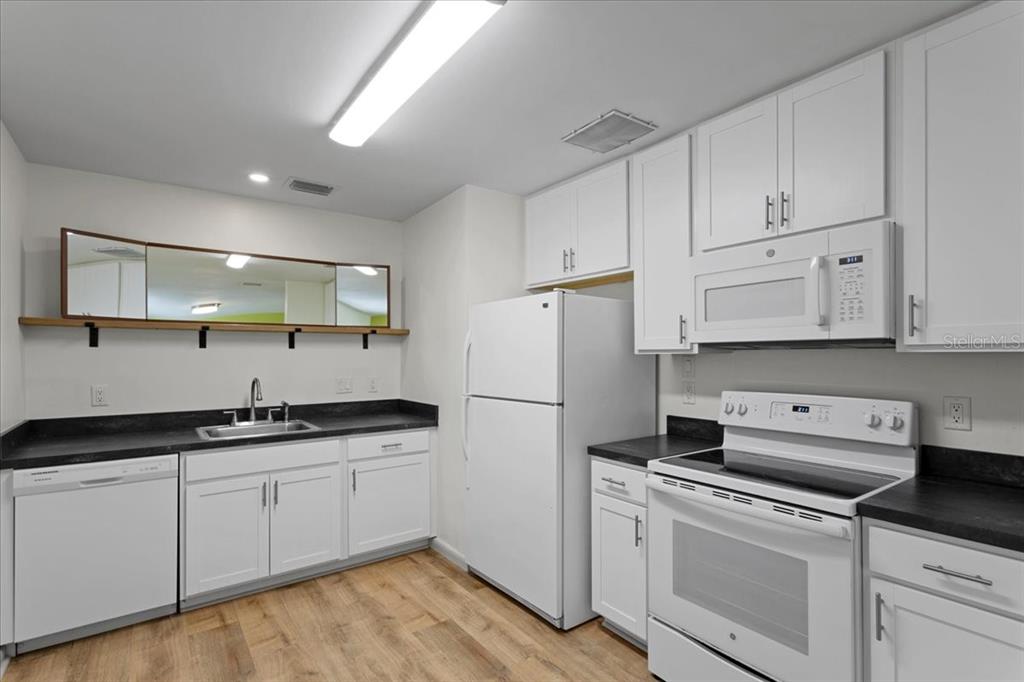 A kitchen with white cabinets, white appliances, dark countertops, and a mirror above the sink — 1302 NE 14TH TERRACE, GAINESVILLE, FL