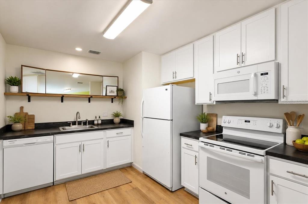 A kitchen features white cabinets, black countertops, white appliances, and a wooden shelf with mirrors — 1302 NE 14TH TERRACE, GAINESVILLE, FL