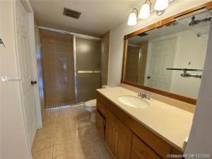 A bathroom features a wooden vanity with a beige countertop, a mirror, and a glass shower — 4166 Inverrary Drive # 303, Lauderhill FL 33319, LAUDERHILL, FL
