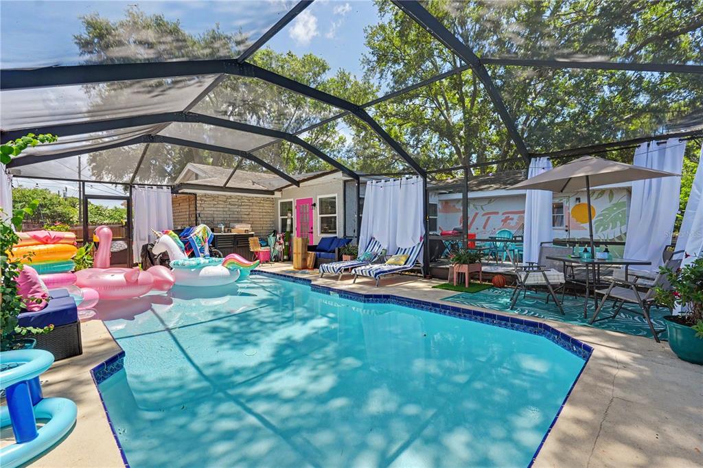 A screened-in swimming pool area features lounge chairs, patio furniture, and various inflatable pool floats — 11208 DUNCAN STREET, SEMINOLE, FL