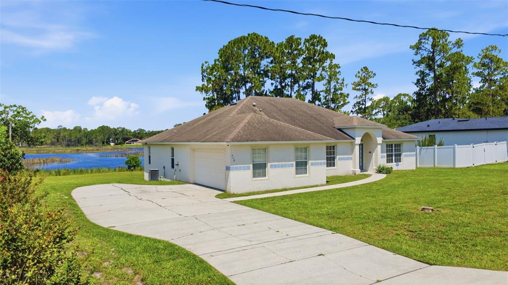 A single-story white house with a concrete driveway sits on a grassy lot near water — 516 GLEN HAVEN DRIVE, DELTONA, FL