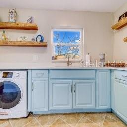 A laundry room features light blue cabinets, a front-load washer, and two floating wooden shelves — 13125 WILCOX ROAD UNIT 5104, LARGO, FL