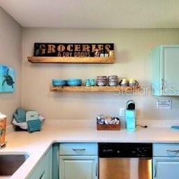 A kitchen features light blue cabinets, white countertops, and two wooden floating shelves on the wall — 13125 WILCOX ROAD UNIT 5104, LARGO, FL