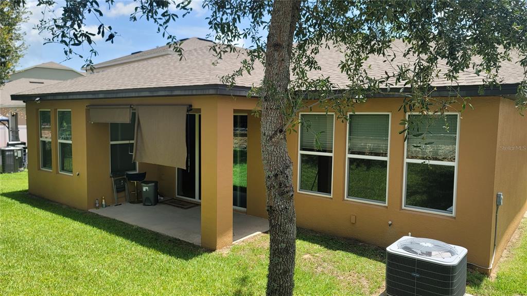 The exterior of a tan house features a covered patio, large windows, and an AC unit — 920 BOXELDER AVENUE, MINNEOLA, FL