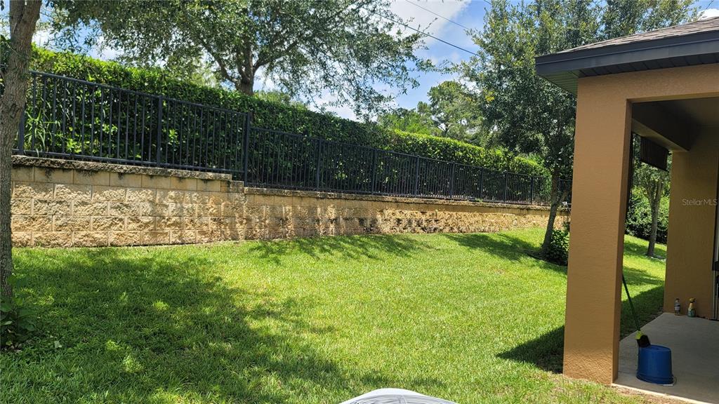 A grassy backyard features a stone retaining wall topped by a black metal fence — 920 BOXELDER AVENUE, MINNEOLA, FL