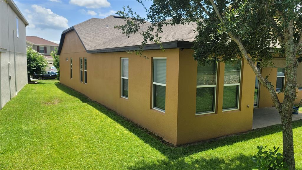 The exterior side and rear view of a tan stucco house with a shingled roof — 920 BOXELDER AVENUE, MINNEOLA, FL